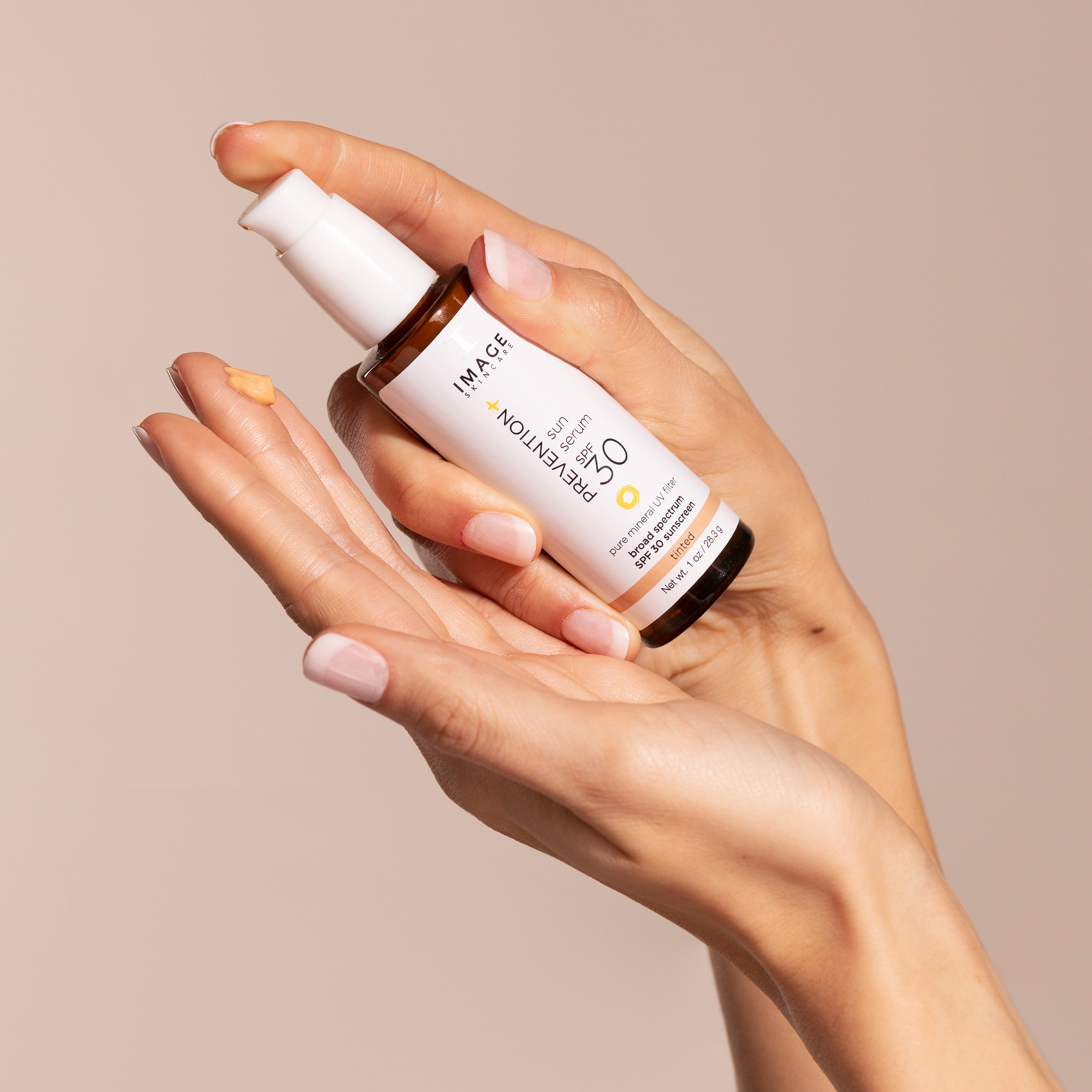 Een close-up van handen die de IMAGE Skincare PREVENTION+ Sun Serum SPF 30 Tinted flacon vasthouden, met een kleine hoeveelheid van de getinte vloeistof op een vingertop.