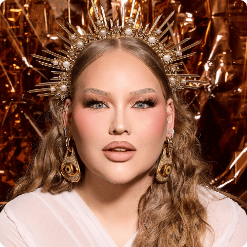NikkieTutorials draagt een gouden kroon en statement oorbellen bij een glamoureuze Nimya make-up look.