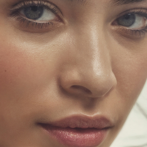 Close-up van het gezicht van een vrouw met een gezonde, stralende huid. De focus ligt op de textuur van de huid rondom de neus, ogen en lippen, wat het resultaat van een goede huidverzorgingsroutine accentueert.