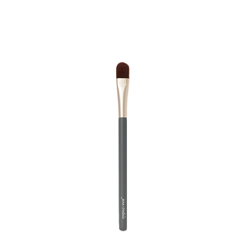 Een Jane Iredale Camouflage Brush op een witte achtergrond. De kwast heeft een donkergrijze steel met het Jane Iredale logo, een goudkleurige huls en een platte, afgeronde donkere borstelkop voor concealer