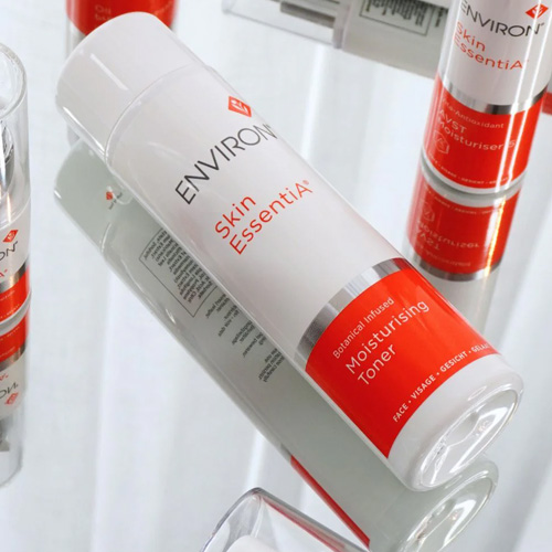 Een close-up van de Environ Skin EssentiA Botanical Infused Moisturising Toner flacon, liggend op een spiegelende ondergrond waarin andere Environ verpakkingen reflecteren.