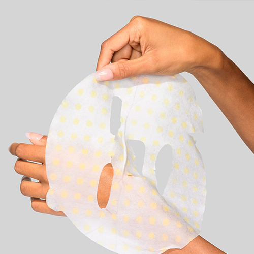 Handen die het sheetmasker met gele stippen vasthouden en ontplooien.