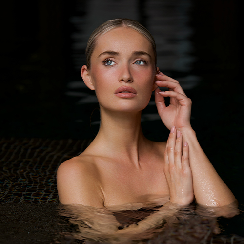 Een vrouw met een verzorgde, gehydrateerde huid kijkt omhoog terwijl ze in het water staat, wat een fris en verjongend gevoel uitstraalt.