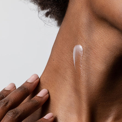 Close-up van een hand die een witte hydraterende crème aanbrengt op de nek van een model met een donkere huidskleur