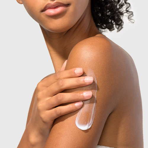 Een model brengt de witte HydroPeptide Lumifirm crème aan op haar schouder en arm