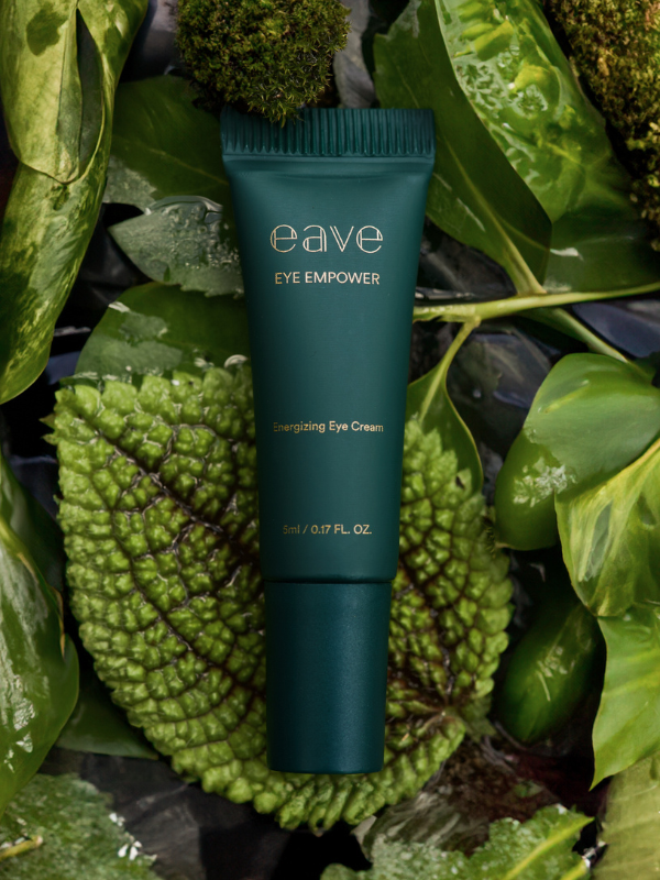 Een donkergroene tube EAVE Eye Empower Energizing Eye Cream liggend op een bed van groene bladeren en mos.