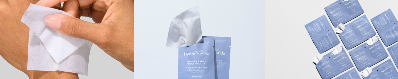 Close-up van twee lichtblauwe sachets van HydroPeptide Resurface & Repair Peptide Pads. Het voorste zakje toont 'Step 1' voor een AHA/BHA/PHA chemische peeling, waaruit een wit exfoliërend doekje steekt. Het achterste zakje toont 'Step 2'.