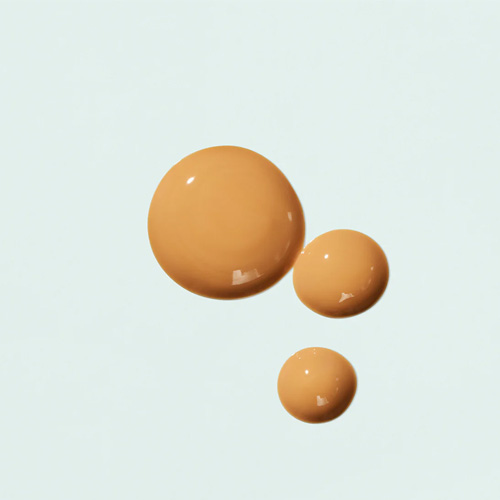 Drie ronde druppels van het getinte IMAGE Skincare PREVENTION+ Sun Serum SPF 30 op een lichtblauwe ondergrond, tonend de glanzende en vloeibare consistentie.