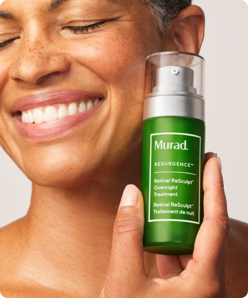 Glimlachende persoon die een groene Murad Retinal ReSculpt Overnight Treatment flacon vasthoudt