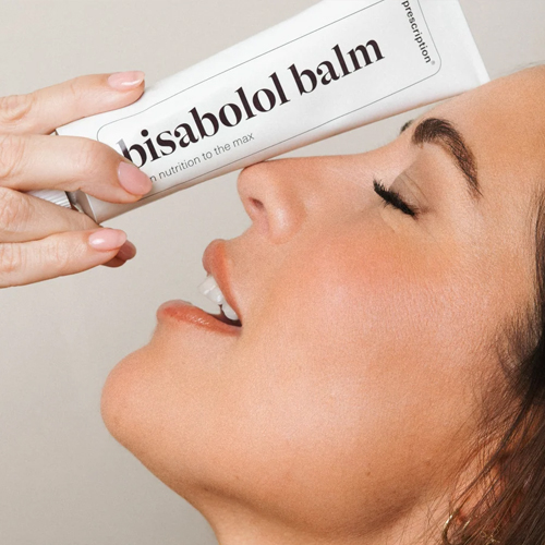 Vrouw die de witte tube Prescription bisabolol balm nabij haar gezicht houdt
