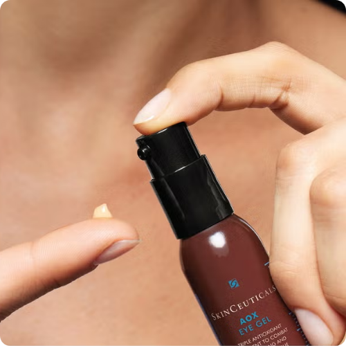 Close-up van een hand die de pomp van een flacon SkinCeuticals AOX+ Eye Gel indrukt, waarbij een kleine dosering gel op de vingertop terechtkomt.