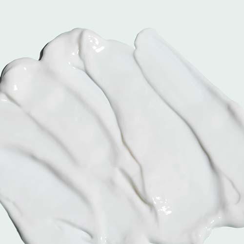 Een close-up van de rijke, romige witte textuur van de Iluma Intense Brightening Crème met zachte uitsmeringen.
