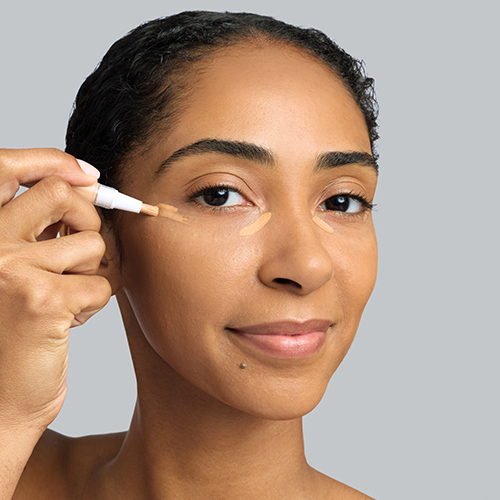 Een vrouw met een getinte huidskleur brengt vloeibare concealer aan onder haar ogen met een applicator pen voor een heldere en egale blik