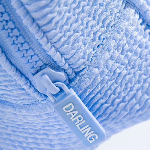 Close-up van de lichtblauwe wafelstof van de Darling toilettas met een ritssluiting voorzien van het Darling logo.