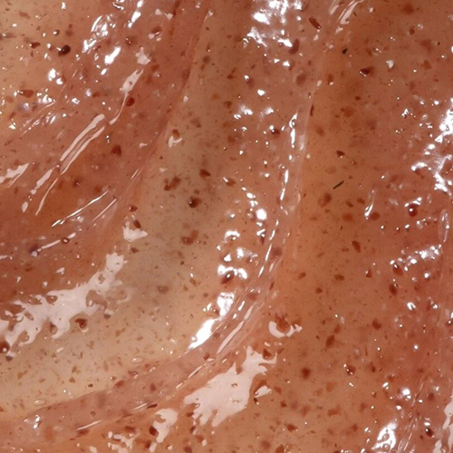 Een gedetailleerde macro-opname die de rijke textuur van de Darling Multi-Biotics Body Scrub laat zien. De scrub is een stroperige, roze-bruine substantie met talloze kleine, donkere scrubdeeltjes erin, die glinstert onder het licht.