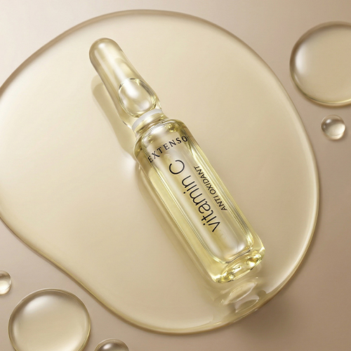 Glazen Extenso vitamin C ampul liggend in een vloeibaar serum met luchtbellen en een gouden gloed