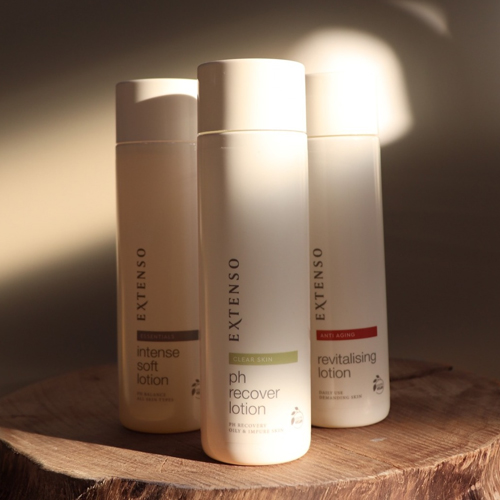Drie verschillende Extenso lotions waaronder de revitalising lotion samen gepresenteerd op een houten ondergrond