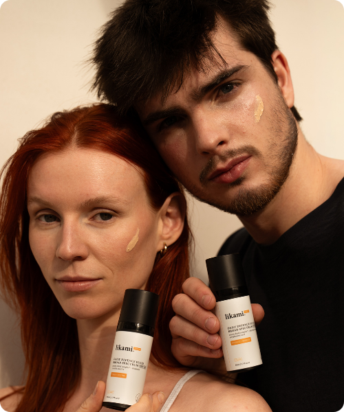 Twee modellen poseren samen met flacons van Likami Daily Defence Fluid, beiden met een beetje van het product op hun wang aangebracht.