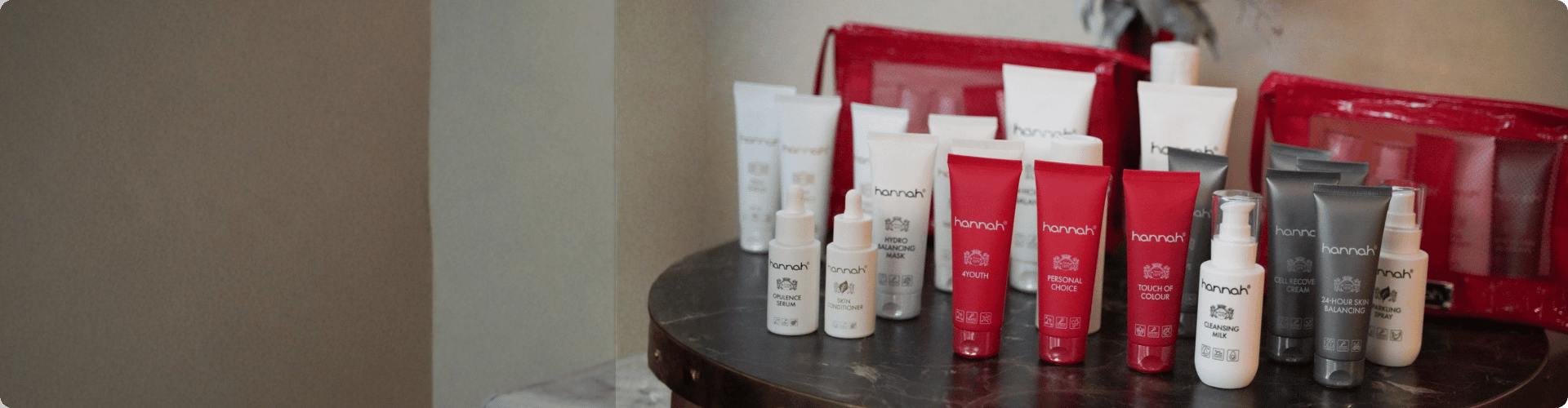 Een overzichtsfoto van diverse hannah-huidverzorgingsproducten, zoals crèmes, serums en lotions, gepresenteerd in rode en witte verpakkingen op een donkere tafel.