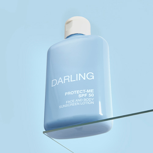 Een blauwe flacon DARLING PROTECT-ME SPF 50 zonnebrandcrème rustend op de rand van een glazen plaat tegen een blauwe lucht.