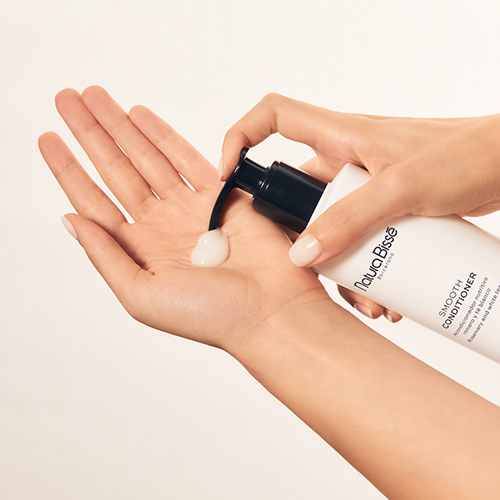 Close-up van een hand die een toefje witte, romige conditioner uit de Natura Bissé fles pompt.