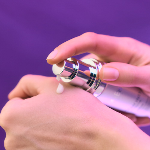 Close-up van handen waarbij een druppel van het Diamond Extreme Serum vanuit de zilveren flacon op de rug van de hand wordt gepompt.