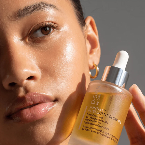 Een model houdt een flesje D-Skin Skintell Intelligent Glow Oil vast naast haar stralende gezicht.