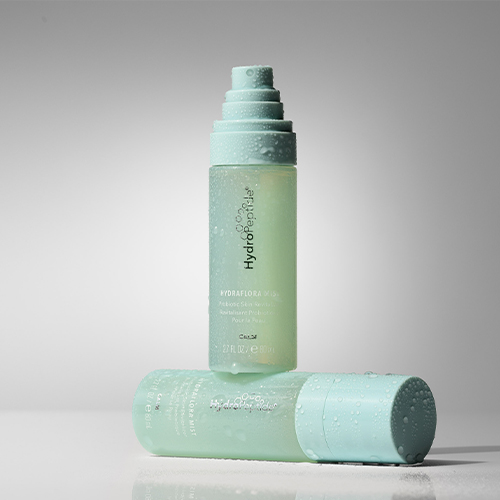 Twee flacons HydroPeptide HydraFlora Mist in een sfeervolle opstelling met waterdruppels
