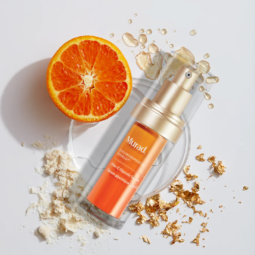 Murad Vita-C Glycolic Serum flacon omringd door een verse sinaasappel en goudvlokken
