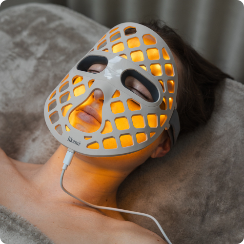 Een persoon ligt ontspannen achterover met het witte Likami LED-masker dat een warme, gele gloed verspreidt. De ogen zijn gesloten en de afbeelding heeft afgeronde hoeken.