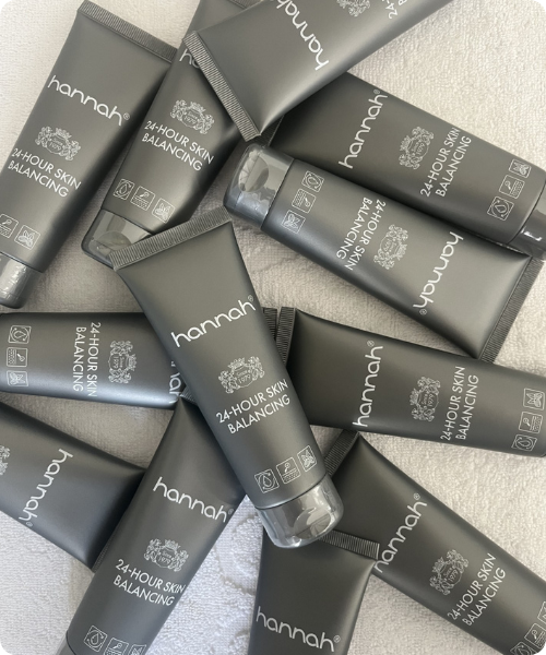 Een bovenaanzicht van een verzameling grijze tubes hannah 24-hour Skin Balancing gezichtscrème, kriskras over elkaar heen liggend op een witte ondergrond.