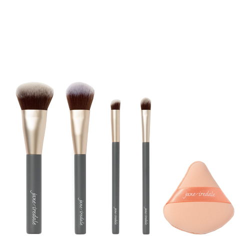 De inhoud van de Jane Iredale Pro Series Essentials Brush Set bestaande uit vier verschillende make-up kwasten met grijze stelen en gouden details naast een perzikkleurige driehoekige make-up spons.