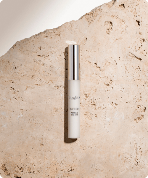 Een slanke flacon Natura Bissé Inhibit Retinol Eye Lift oogverzorging geplaatst op een natuurlijke, ruwe stenen achtergrond.