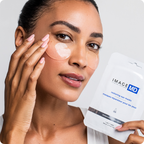 Een vrouw brengt de IMAGE Skincare IMAGE MD restoring eye masks aan onder haar ogen, terwijl ze de verpakking vasthoudt.