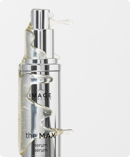 Close-up van het IMAGE Skincare the MAX serum in een zilveren flacon met een transparante, stroperige textuur die over de verpakking loopt.