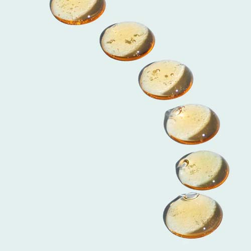 Close-up van transparante, goudkleurige gel-druppels van de Image Skincare Blemish Gel op een lichte achtergrond