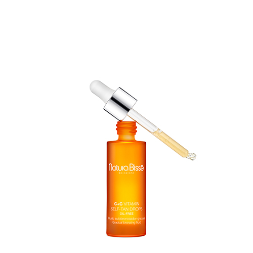 Een geopende flacon van de zelfbruiner druppels waarbij de glazen pipet met vloeistof schuin boven de opening rust.