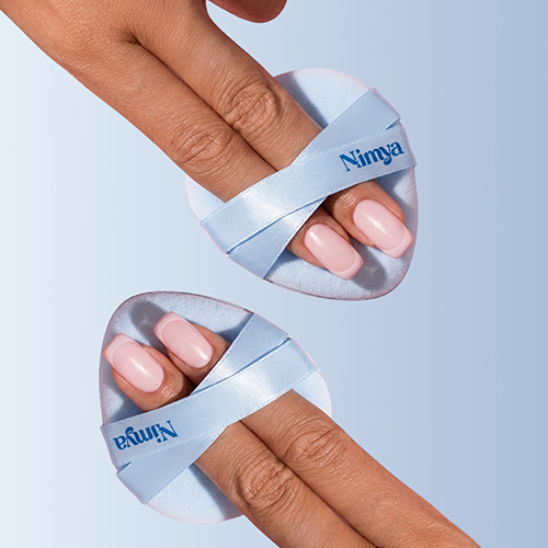 Close-up van twee handen die de Nimya poederdonsjes vasthouden. De vingers glijden door de gekruiste linten, wat laat zien hoe het ontwerp zorgt voor maximale controle.