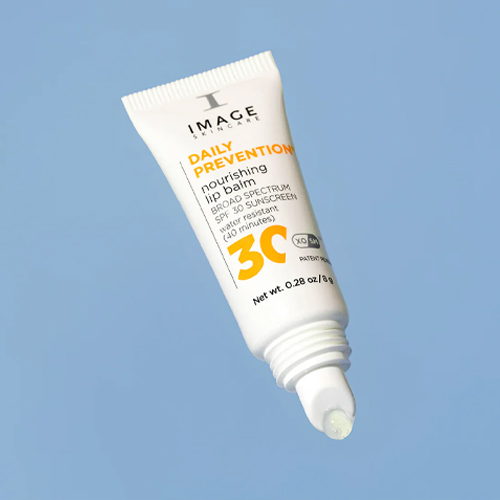 Een geopende tube van de Daily Prevention lipbalm op een blauwe achtergrond, waarbij een druppel van de transparante, glanzende gel uit de applicator komt.