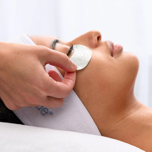 Een schoonheidsspecialist brengt frisse eyepads aan onder de ogen van een ontspannen klant in de salon.