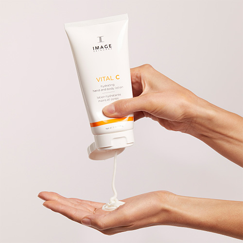 Iemand knijpt de IMAGE Skincare VITAL C Hydrating Hand and Body Lotion vanuit de tube in de palm van hun hand.