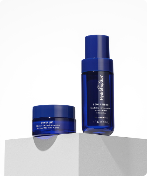 Het HydroPeptide Power Serum en de Power Lift gezichtscrème in donkerblauwe verpakkingen op een minimalistische witte kubus.