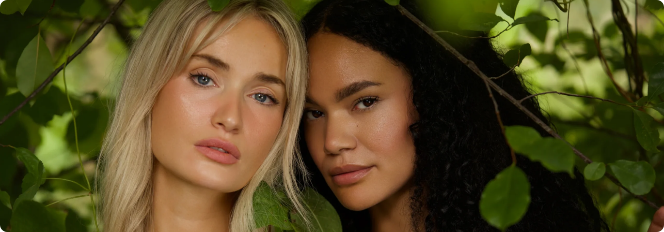 Een close-up portret van twee vrouwen met een stralende huid, omringd door groene bladeren en takken, wat de natuurlijke focus van de Bioquantine®-lijn benadrukt.