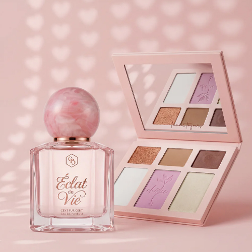 Een stijlvolle set bestaande uit een flesje 'Éclat de Vie' eau de parfum van Cent Pur Cent met een roze marmeren dop, naast een bijpassende Palette d'Amour make-uppalet met verschillende oogschaduw- en blushkleuren in een roze verpakking.