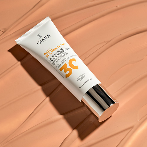 De tube van de Pure Mineral Tinted Moisturizer liggend op een glad uitgesmeerde laag van de getinte zonnebrandcrème.