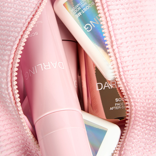 Een close-up shot van de opengevouwen, roze wafel geweven Darling toilettas. In de tas zijn verschillende roze en holografische Darling zonnebrand en huidverzorgingsproducten te zien.