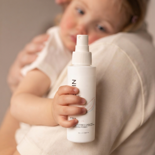 Een peuter wordt vastgehouden door een ouder en houdt een witte flacon met de tekst D-SKIN Baby Mist Oil vast.
