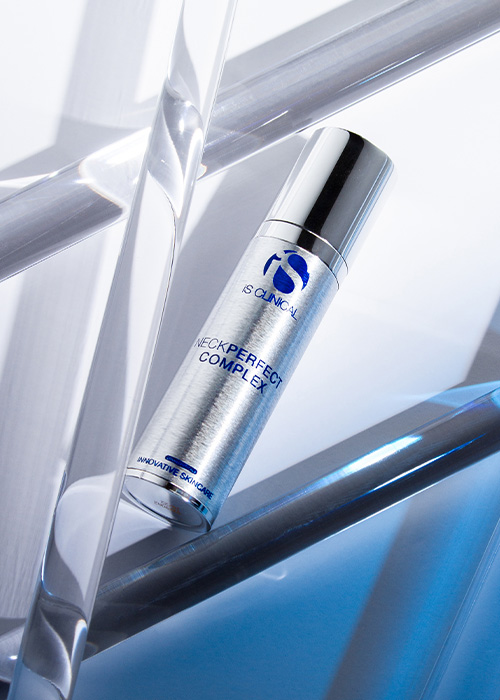 Een flesje iS Clinical Neck Perfect Complex geplaatst tussen transparante glazen of acryl staven tegen een blauw-witte achtergrond.