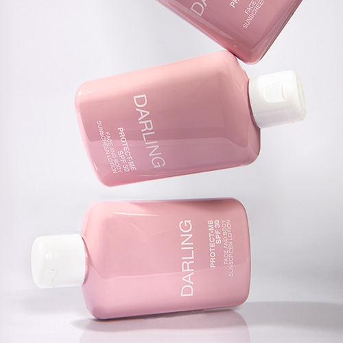 Drie roze flacons van DARLING PROTECT-ME SPF 30 die speels boven elkaar zweven tegen een witte achtergrond.