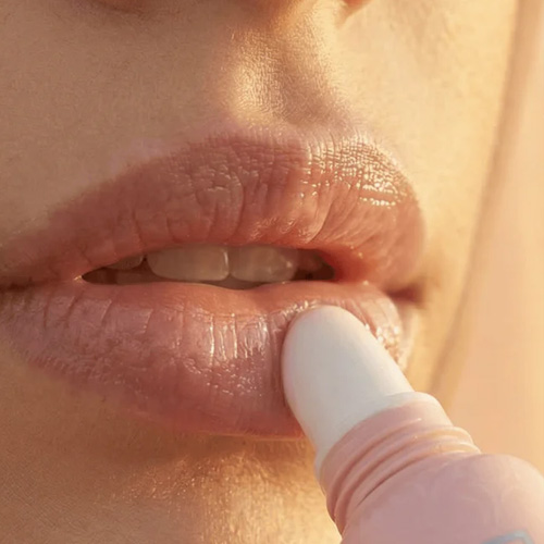 Een close-up van een persoon die de Lip Volume Therapy No. 1 aanbrengt op de lippen met de witte applicator. De lippen hebben een subtiele, gezonde glans door de balsem.